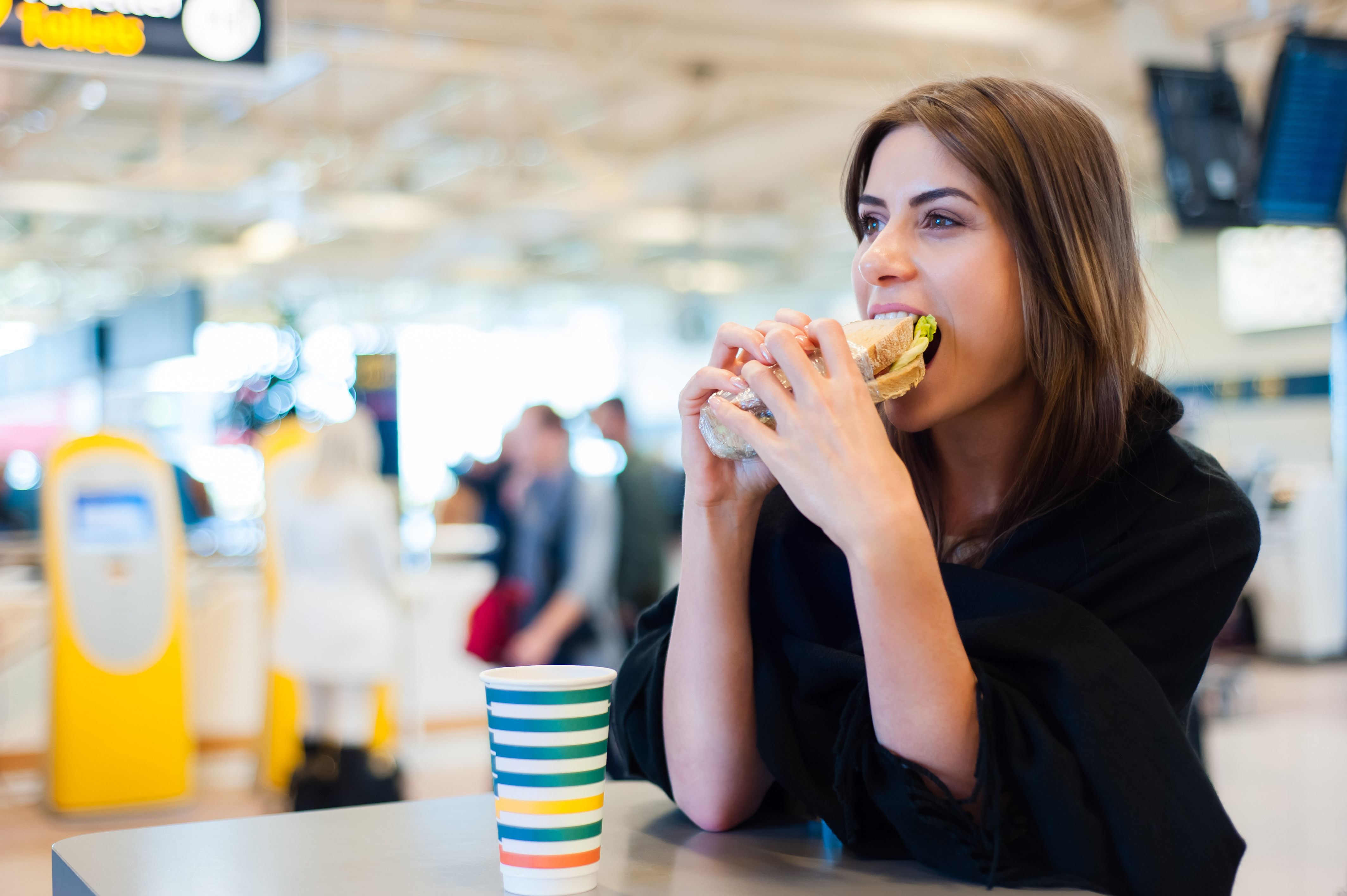 A woman in a black shirt eats a sandwich in an airport restaurant; Best airports for local food