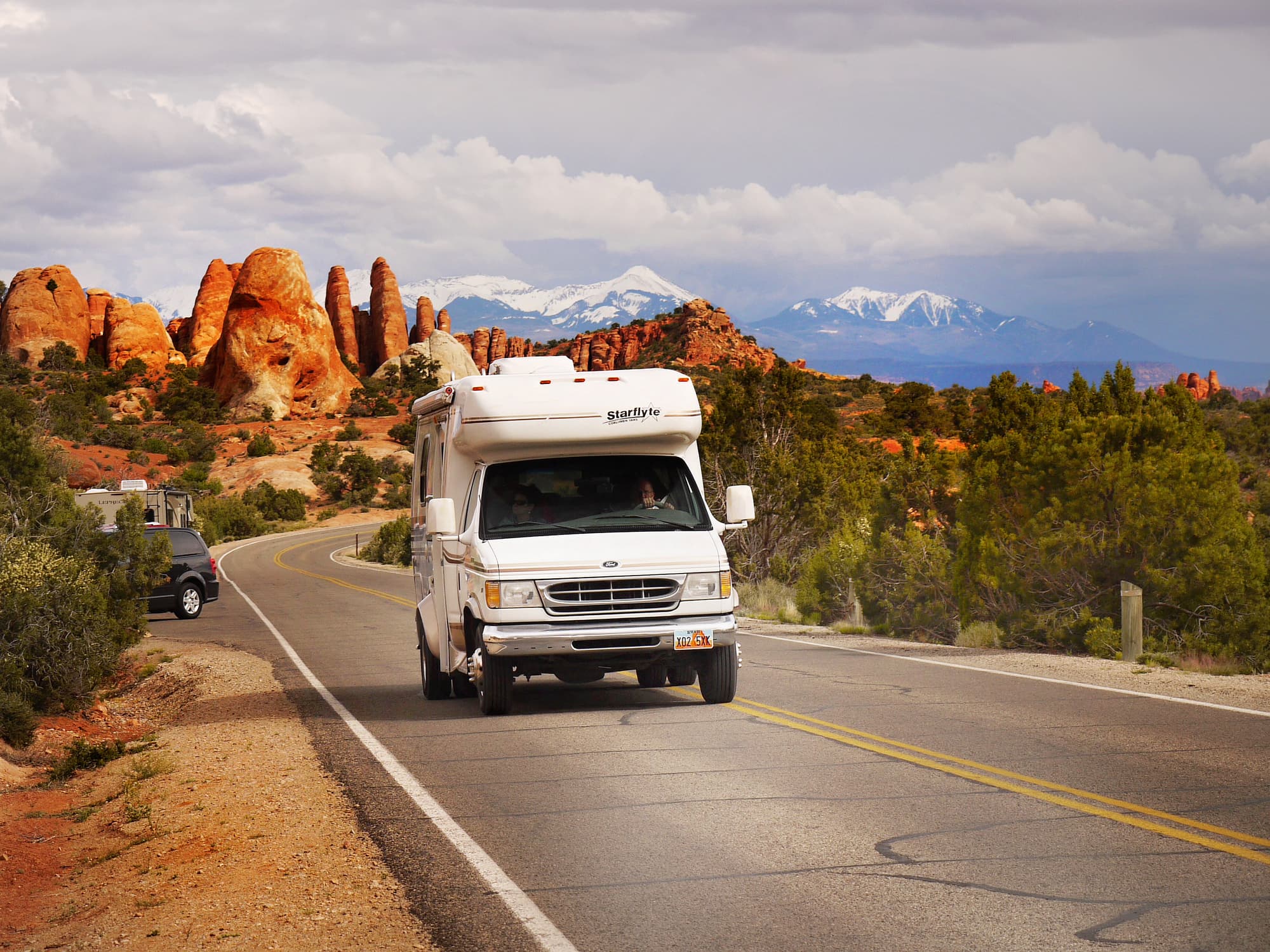 An RV drives past red rocks in Arches National Park, Utah.