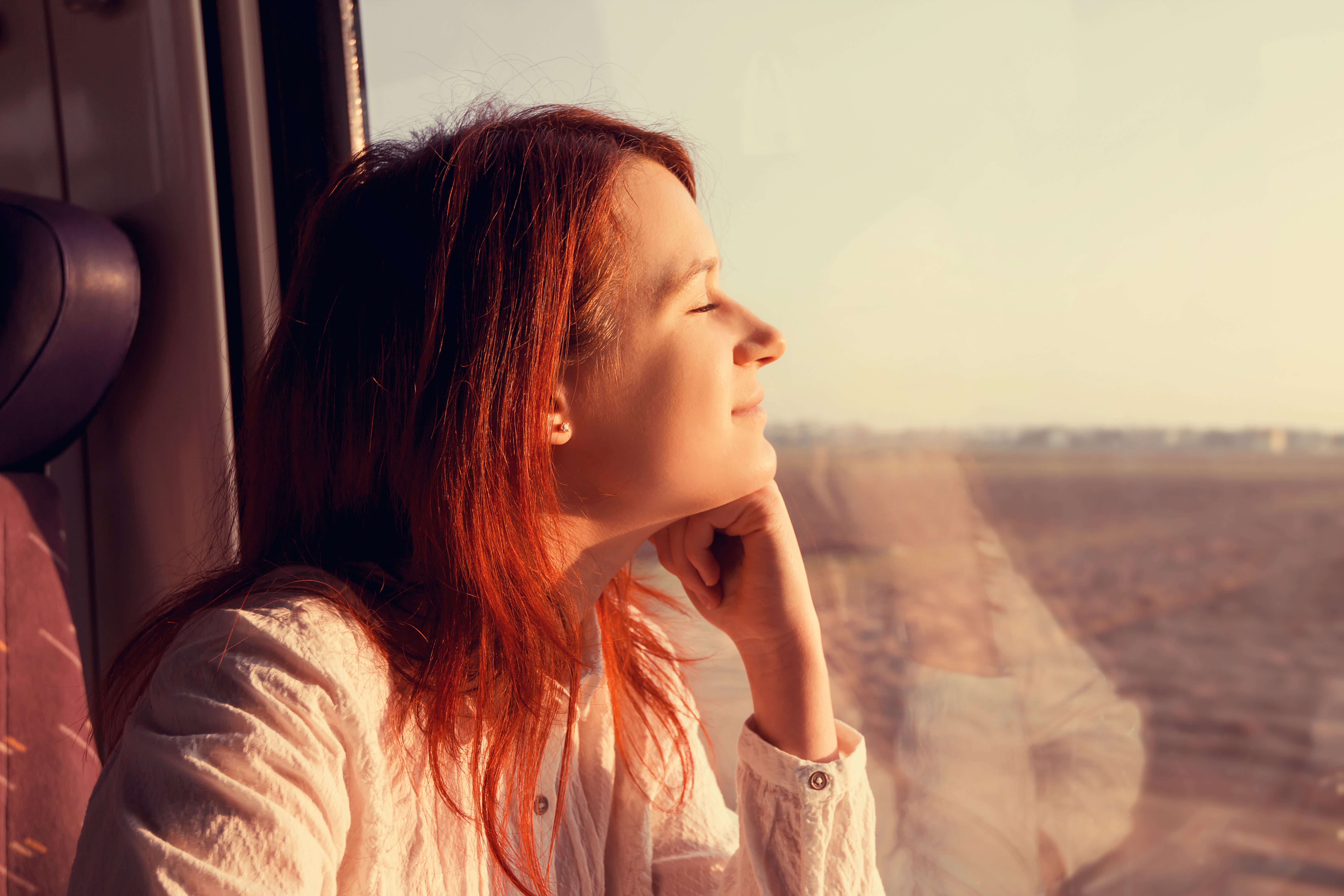 A young woman looks relaxed and satisfied as she looks out a train window while traveling