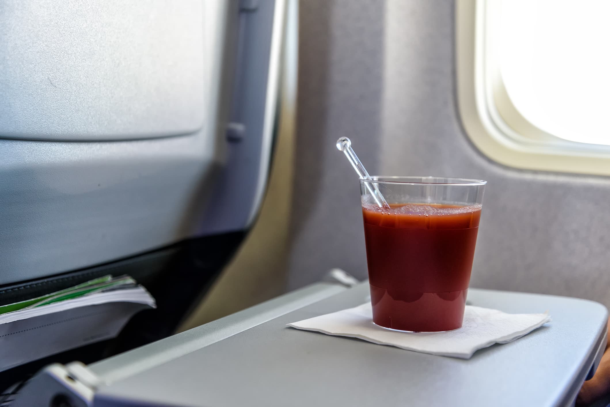 A view of a glass of tomato juice on an airplane tray.