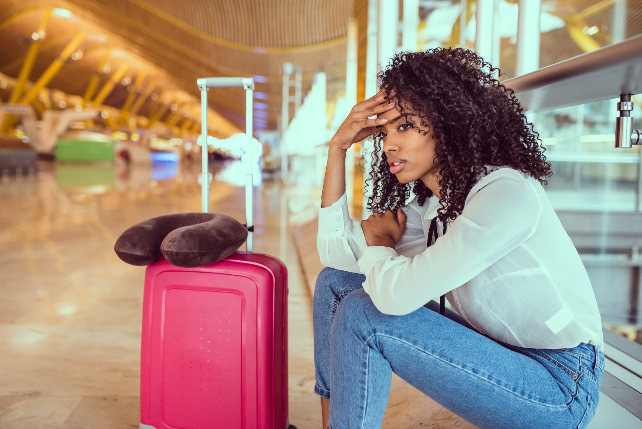 View of a woman sitting at an airport baggage carousel looking frustrated.
