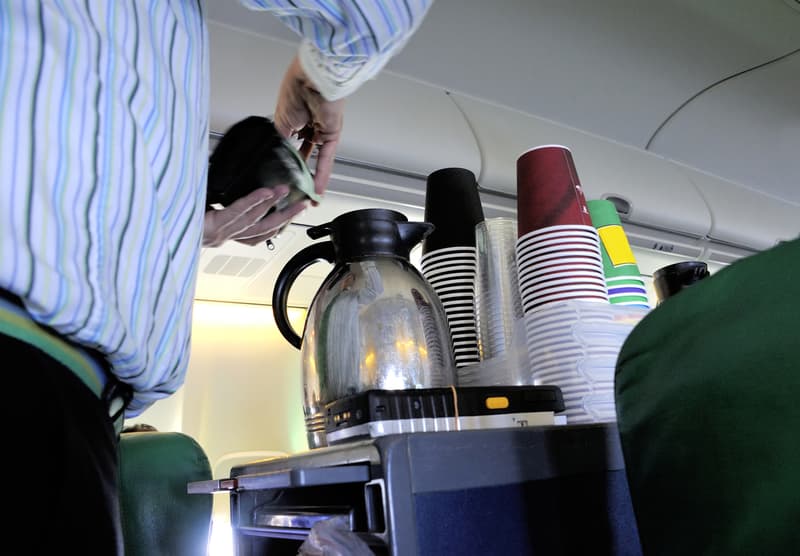 A view of a flight attending pouring coffee from a cart.
