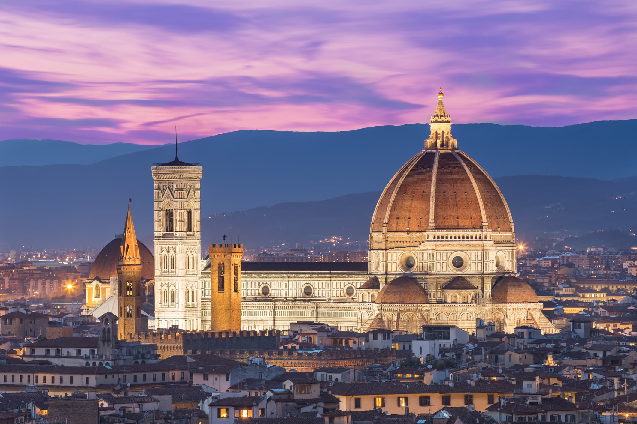 A panoramic view of Florence, Italy, with the Duomo and mountains in the background.