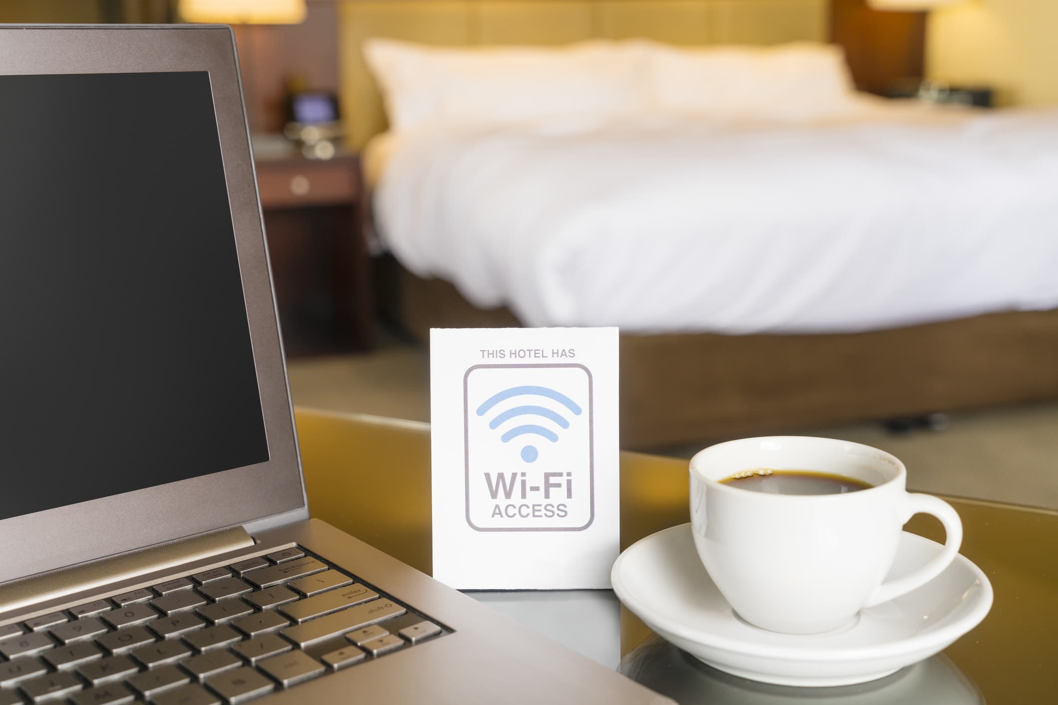A hotel desk with laptop, cup of coffee, and wi-fi sign