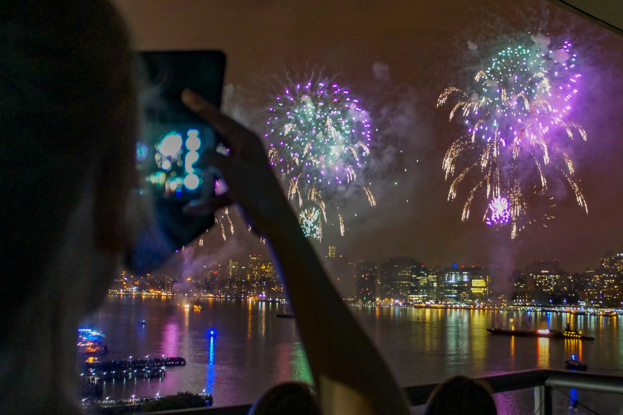 A view of New York City's 4th of July fireworks with a cellphone photographer in the foreground.